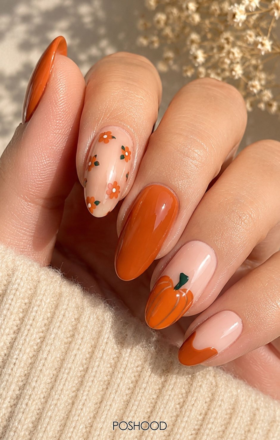 Almond-shaped French tip nails with miniature orange pumpkins, delicate vines, and tiny autumn leaves against a warm fall background.