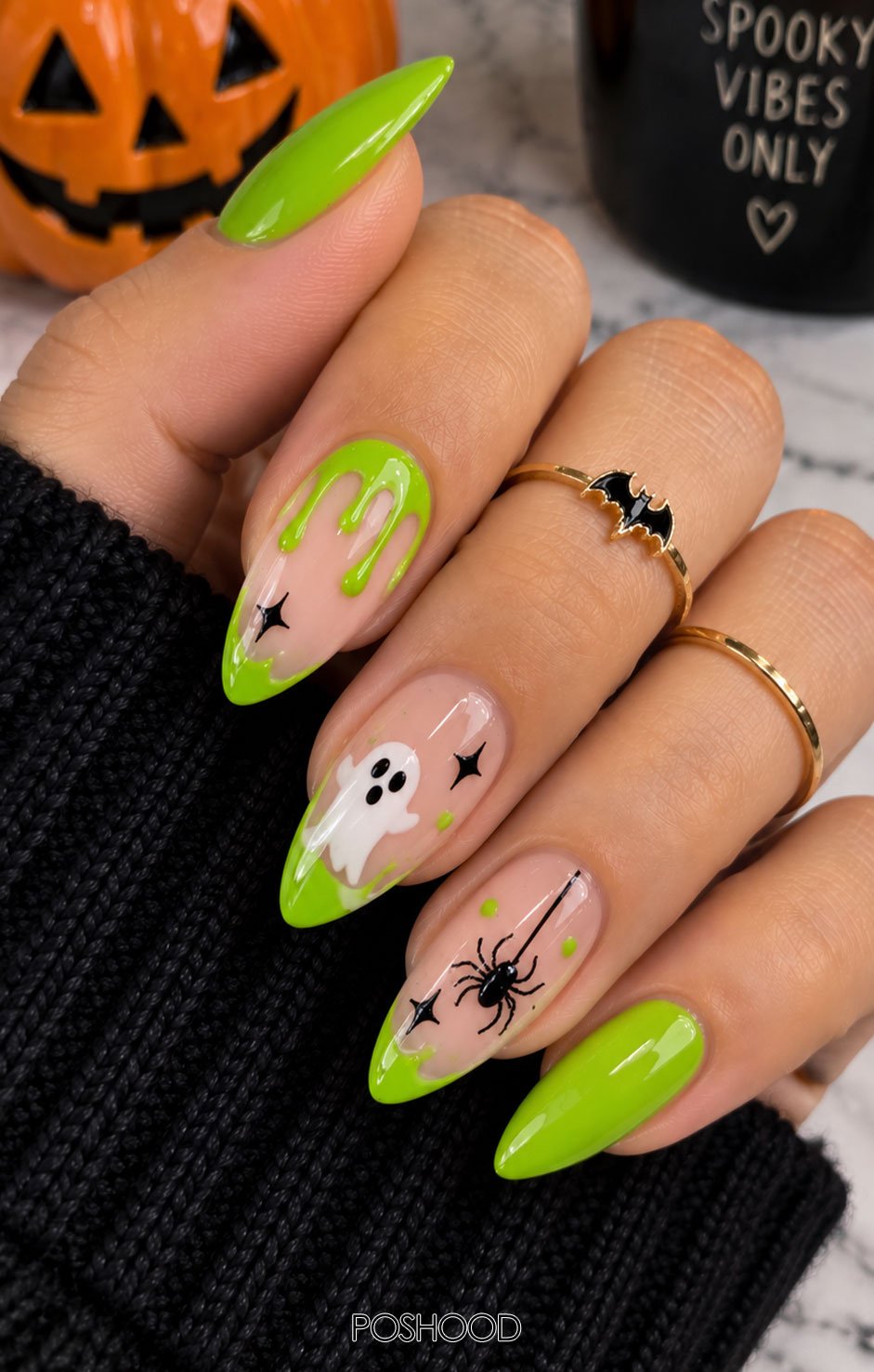 Glossy lime green almond-shaped Halloween nails featuring dripping slime designs, tiny eyeballs, black spiders, and glitter accents against a colorful Halloween background.
