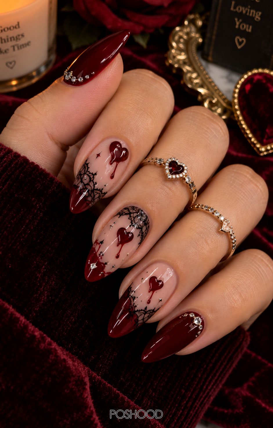 Glossy deep burgundy almond-shaped Halloween nails featuring dripping hearts, black lace details, and crystal embellishments against a luxurious velvet background.