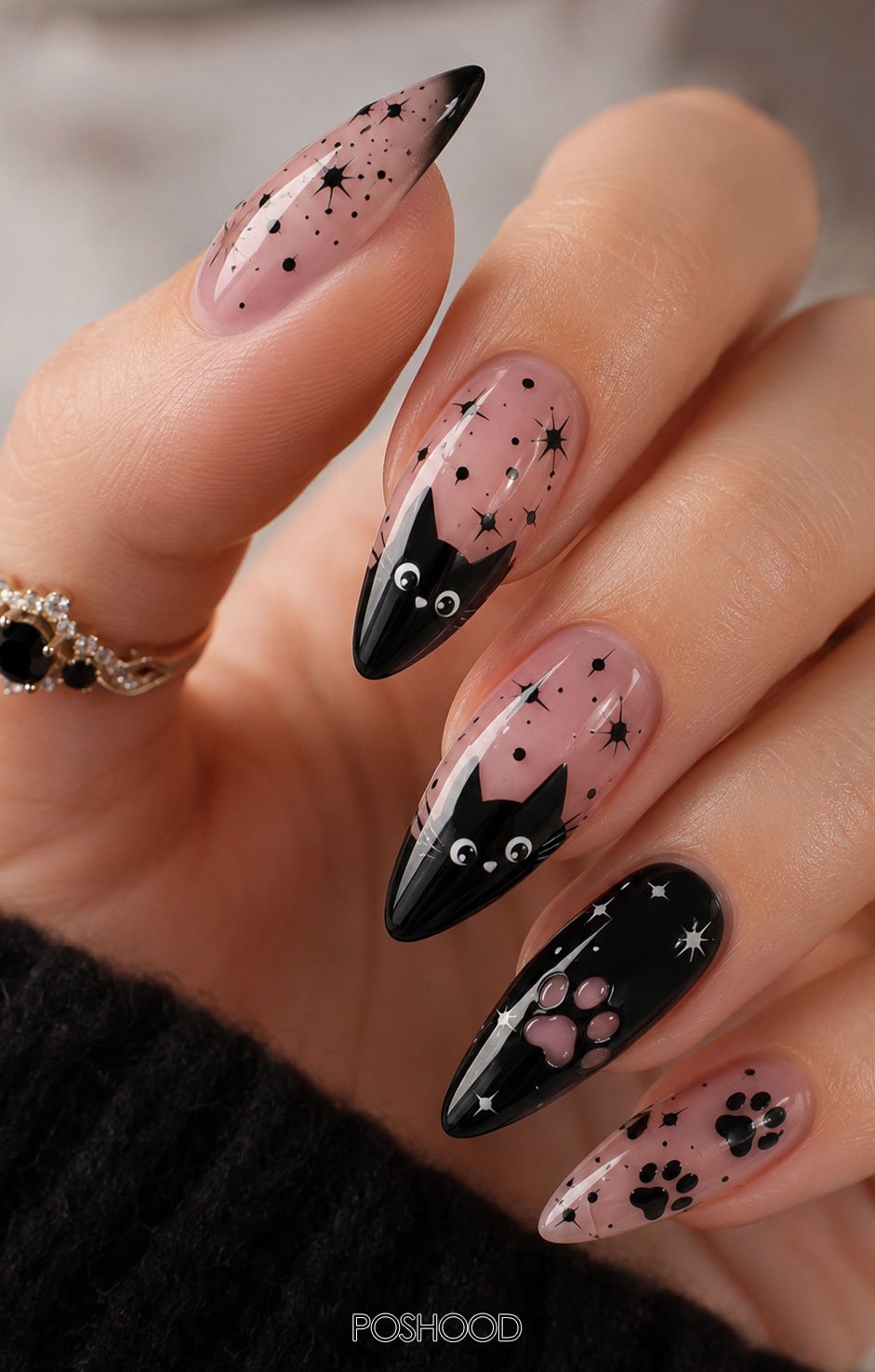 Glossy nude pink almond-shaped Halloween nails featuring adorable black cat faces, tiny stars, black paw prints, and glossy black accent nails.