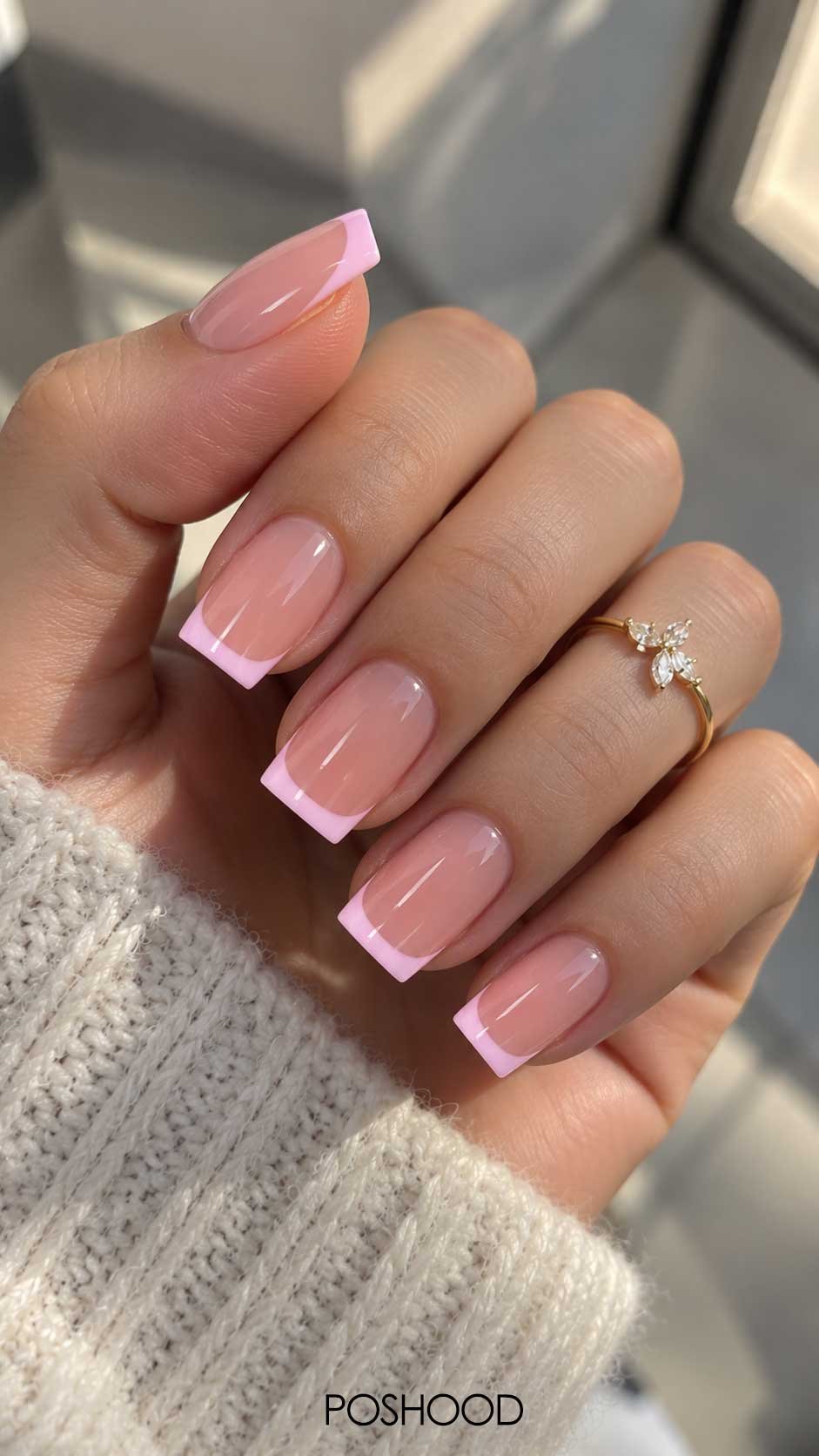 Soft pink glossy French tip nails on a hand with delicate pink tips and a gold floral ring