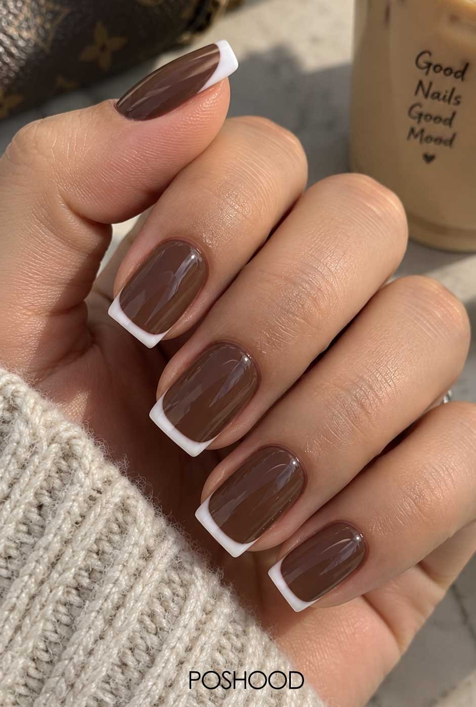 Glossy chocolate brown nails with crisp white French tips and a cozy neutral sweater